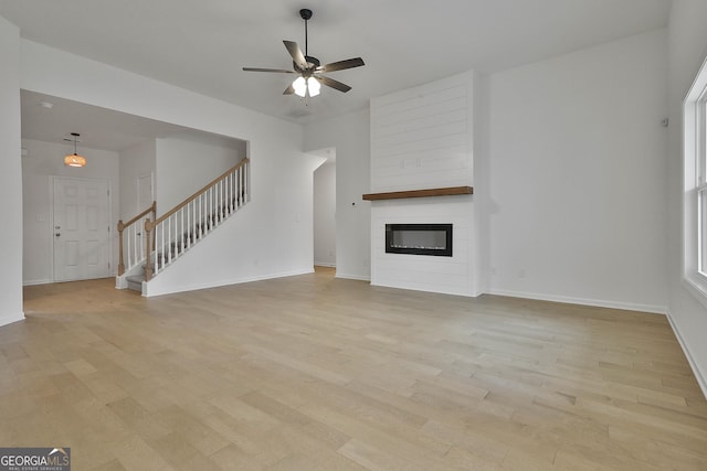 unfurnished living room with ceiling fan, a large fireplace, and light wood-type flooring