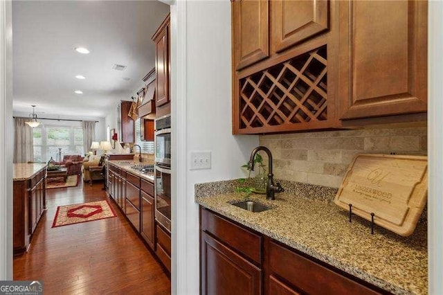 kitchen featuring sink, decorative light fixtures, dark hardwood / wood-style floors, light stone countertops, and backsplash