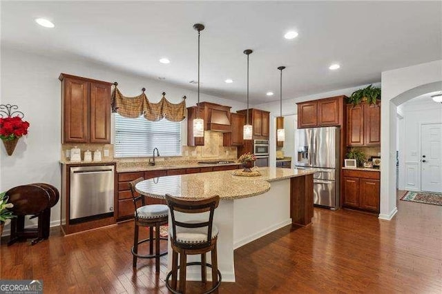 kitchen with appliances with stainless steel finishes, hanging light fixtures, a kitchen island, dark hardwood / wood-style flooring, and decorative backsplash