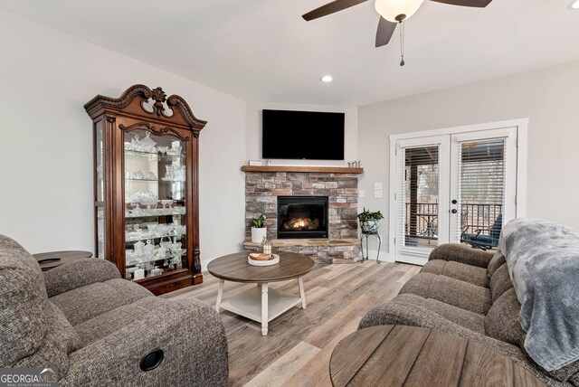 living room featuring french doors, ceiling fan, a stone fireplace, and light wood-type flooring