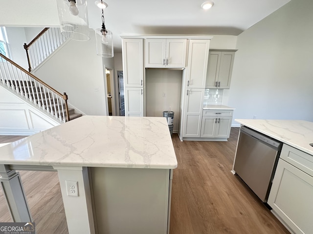 kitchen with light hardwood / wood-style flooring, dishwasher, tasteful backsplash, light stone countertops, and decorative light fixtures