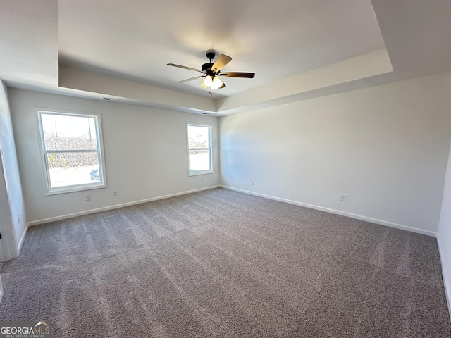 carpeted empty room with plenty of natural light, ceiling fan, and a tray ceiling