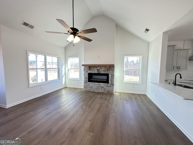 unfurnished living room featuring vaulted ceiling, a stone fireplace, sink, dark hardwood / wood-style flooring, and ceiling fan