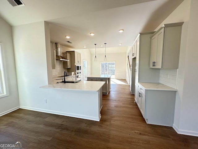 kitchen featuring wall chimney exhaust hood, decorative light fixtures, dark hardwood / wood-style floors, kitchen peninsula, and decorative backsplash