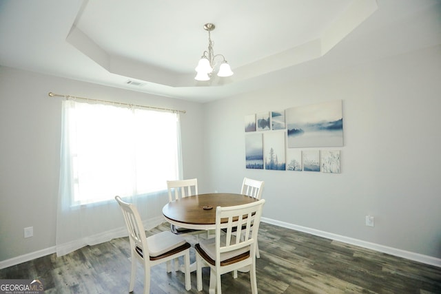 dining area with an inviting chandelier, dark wood-type flooring, and a raised ceiling