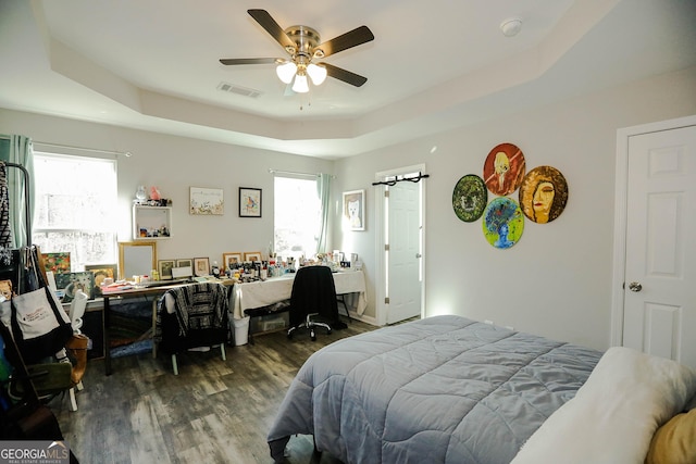 bedroom with multiple windows, dark hardwood / wood-style floors, a raised ceiling, and ceiling fan