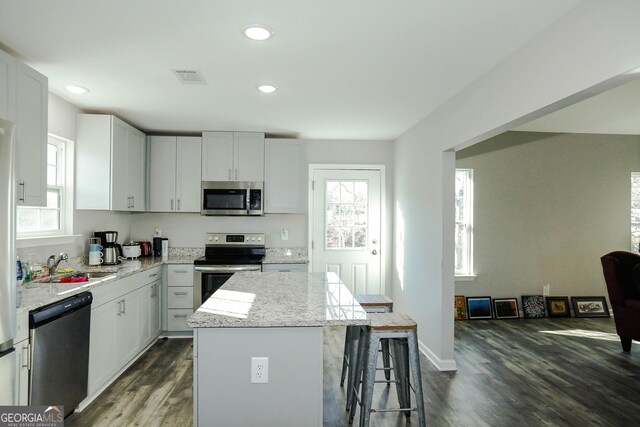 kitchen featuring sink, white cabinetry, a center island, appliances with stainless steel finishes, and light stone countertops