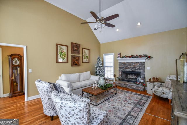 living room featuring ceiling fan, wood-type flooring, a stone fireplace, and high vaulted ceiling