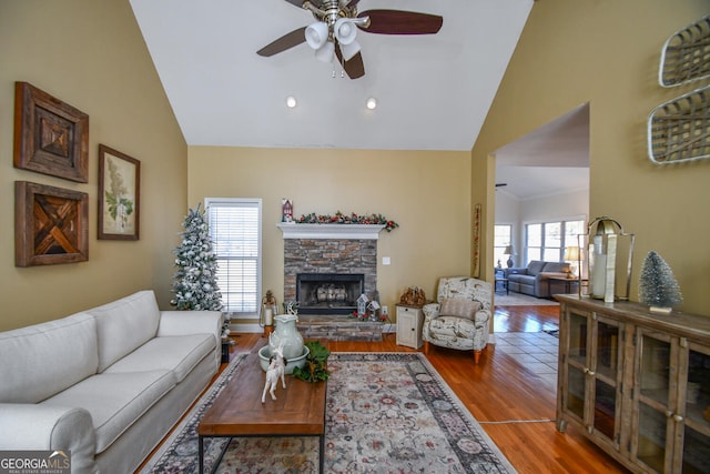 living room with hardwood / wood-style flooring, ceiling fan, high vaulted ceiling, and a fireplace