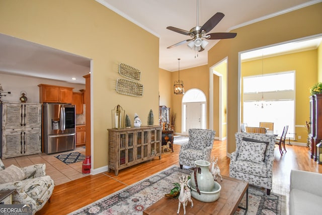 living room with crown molding, a towering ceiling, ceiling fan, and light wood-type flooring