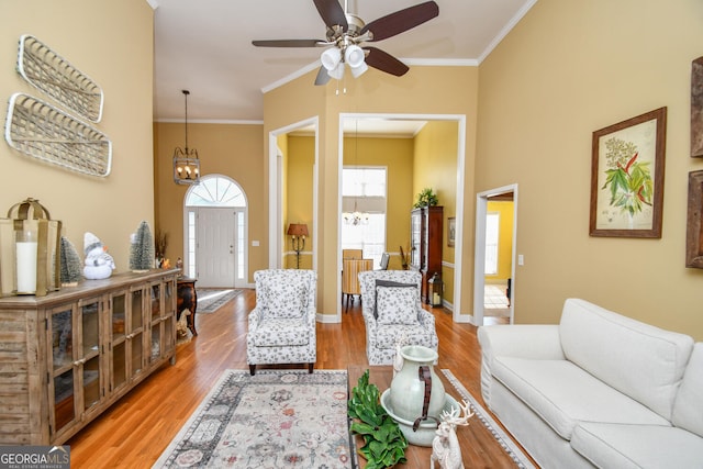 living room with crown molding, ceiling fan with notable chandelier, and light wood-type flooring