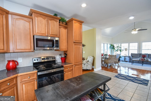 kitchen featuring vaulted ceiling, decorative backsplash, light tile patterned floors, ceiling fan, and stainless steel appliances