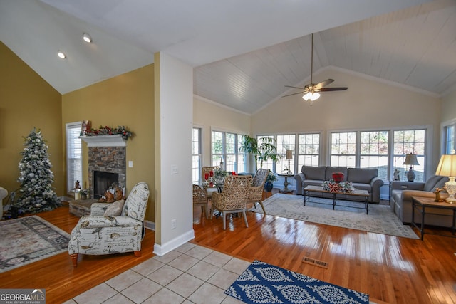 tiled living room featuring a stone fireplace, high vaulted ceiling, and ceiling fan