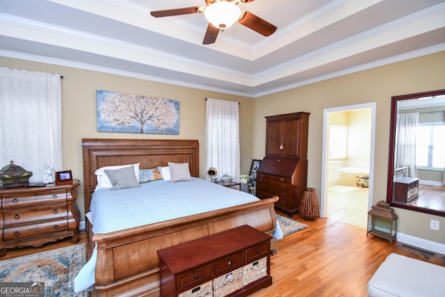 bedroom featuring ornamental molding, ceiling fan, a tray ceiling, ensuite bath, and light hardwood / wood-style flooring