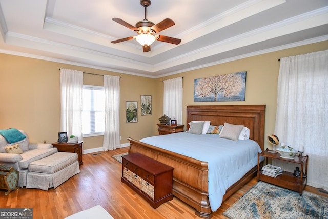 bedroom with crown molding, a raised ceiling, ceiling fan, and light wood-type flooring