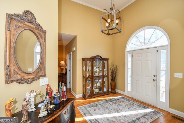 foyer with crown molding, a chandelier, hardwood / wood-style floors, and a high ceiling