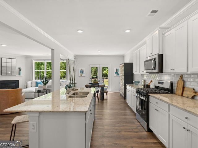 kitchen featuring sink, appliances with stainless steel finishes, white cabinetry, a kitchen island with sink, and light stone counters