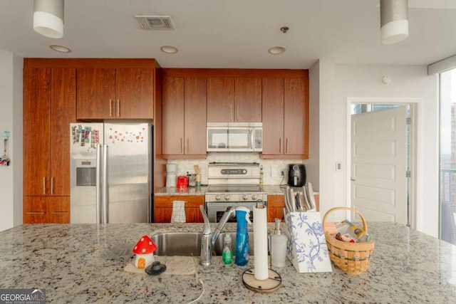 kitchen with appliances with stainless steel finishes, sink, light stone counters, and decorative backsplash