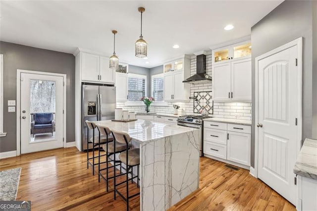 kitchen with appliances with stainless steel finishes, decorative light fixtures, white cabinets, a center island, and wall chimney range hood