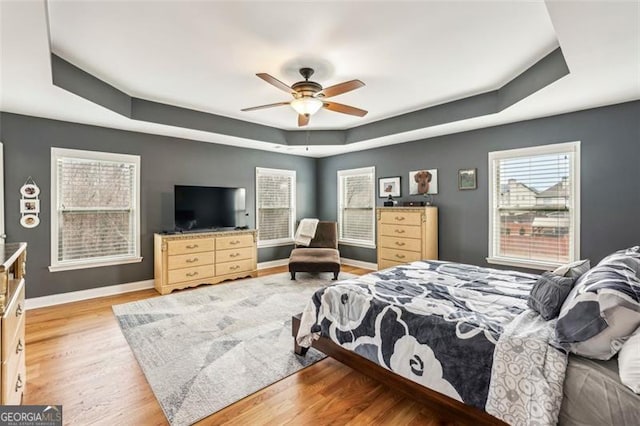 bedroom featuring light wood-type flooring, ceiling fan, and a tray ceiling