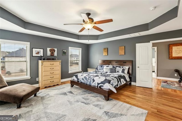 bedroom featuring multiple windows, a tray ceiling, wood-type flooring, and ceiling fan