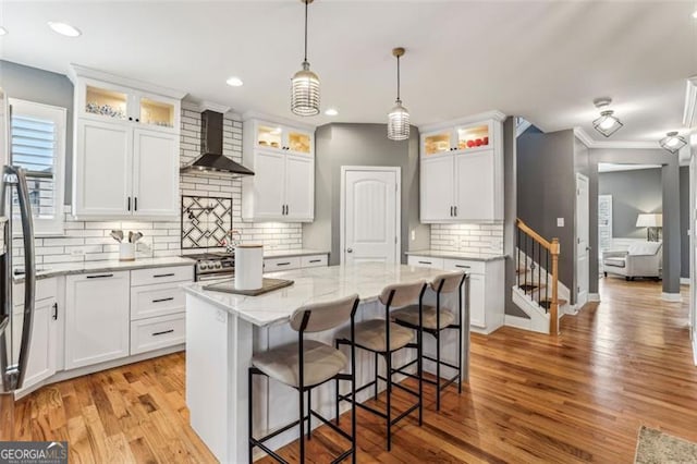 kitchen with white cabinetry, a center island, wall chimney range hood, and backsplash