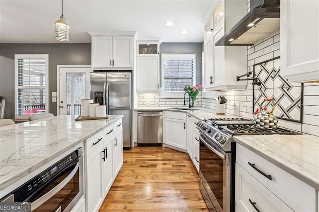 kitchen with white cabinetry, stainless steel appliances, decorative light fixtures, and wall chimney range hood