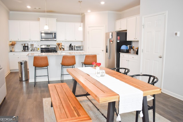 kitchen with pendant lighting, a breakfast bar area, stainless steel appliances, white cabinets, and a center island with sink