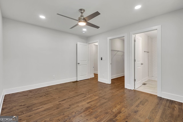 unfurnished bedroom with dark wood-type flooring, ceiling fan, connected bathroom, a walk in closet, and a closet