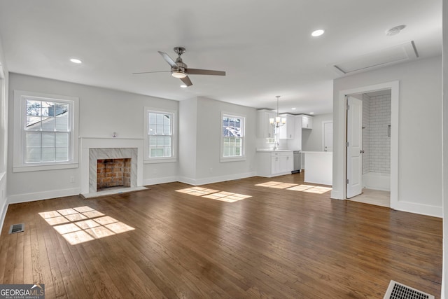 unfurnished living room with ceiling fan with notable chandelier, a healthy amount of sunlight, dark wood-type flooring, and a fireplace