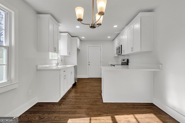 kitchen with appliances with stainless steel finishes, sink, white cabinets, hanging light fixtures, and dark wood-type flooring