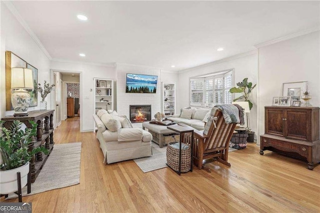 living room featuring crown molding, a fireplace, built in features, and light hardwood / wood-style flooring