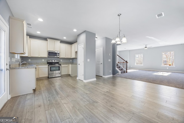 kitchen featuring light stone counters, appliances with stainless steel finishes, light hardwood / wood-style floors, and pendant lighting