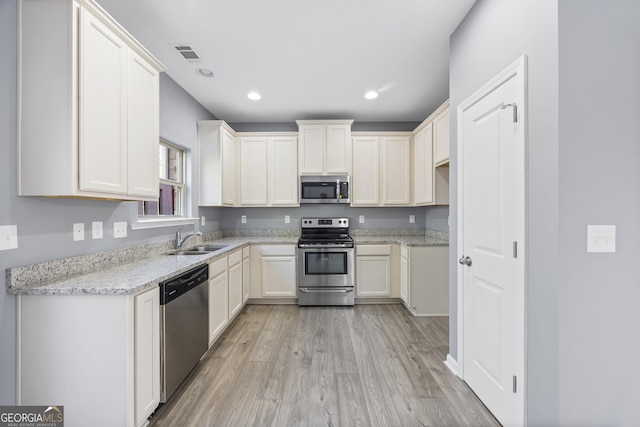 kitchen with light stone counters, appliances with stainless steel finishes, sink, and light wood-type flooring