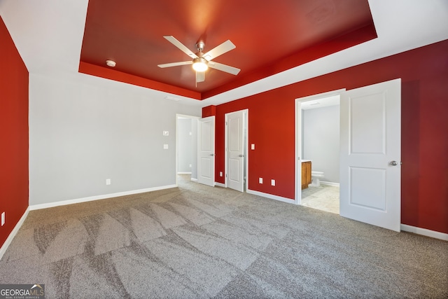 unfurnished bedroom featuring ceiling fan, a tray ceiling, light colored carpet, and ensuite bath