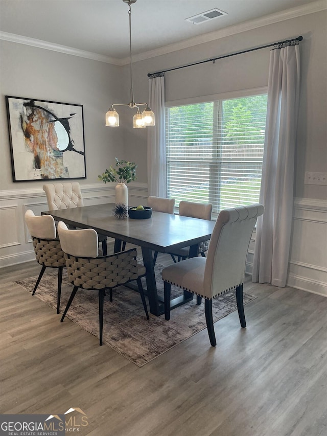 dining space with wood-type flooring, ornamental molding, and a chandelier