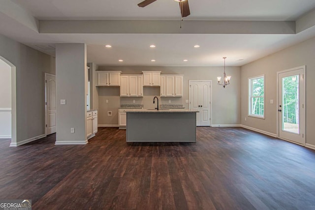 kitchen featuring white cabinetry, sink, dark hardwood / wood-style flooring, light stone counters, and a center island with sink