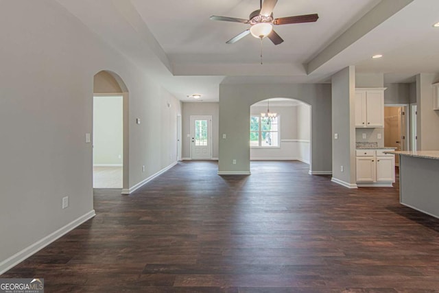 unfurnished living room featuring a tray ceiling, dark wood-type flooring, and ceiling fan with notable chandelier