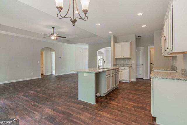 kitchen with dark hardwood / wood-style floors, an island with sink, pendant lighting, light stone countertops, and white cabinets