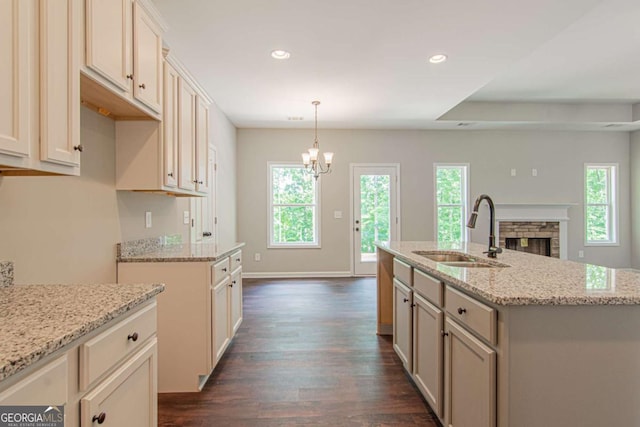 kitchen featuring sink, dark hardwood / wood-style flooring, pendant lighting, light stone countertops, and a kitchen island with sink