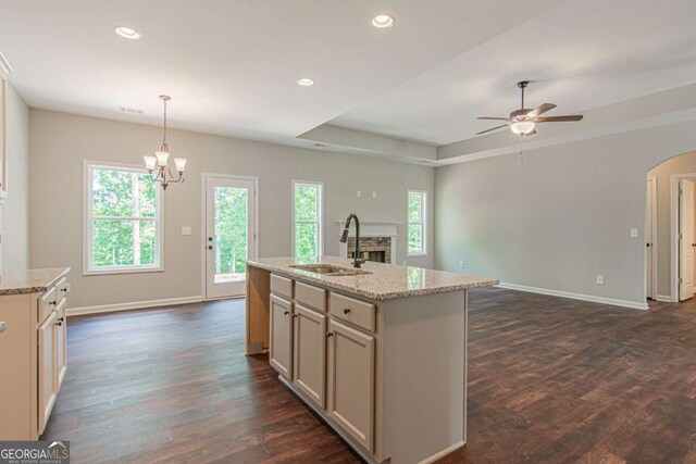 kitchen with dark hardwood / wood-style floors, sink, hanging light fixtures, a kitchen island with sink, and light stone counters