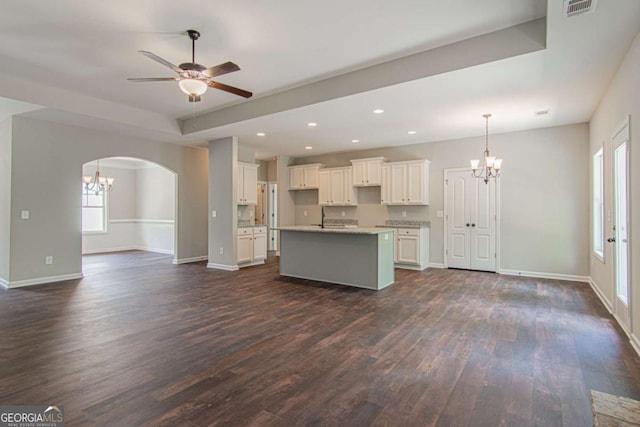 kitchen with white cabinetry, ceiling fan with notable chandelier, dark hardwood / wood-style flooring, and an island with sink