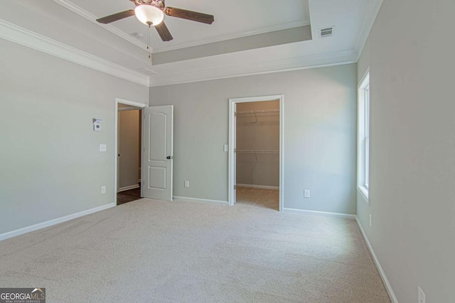 unfurnished bedroom with a tray ceiling, ornamental molding, light colored carpet, and a spacious closet