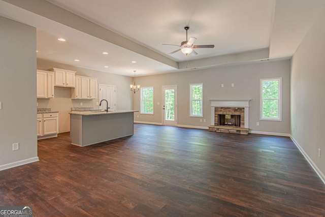 unfurnished living room featuring dark hardwood / wood-style floors, a tray ceiling, a stone fireplace, and a wealth of natural light