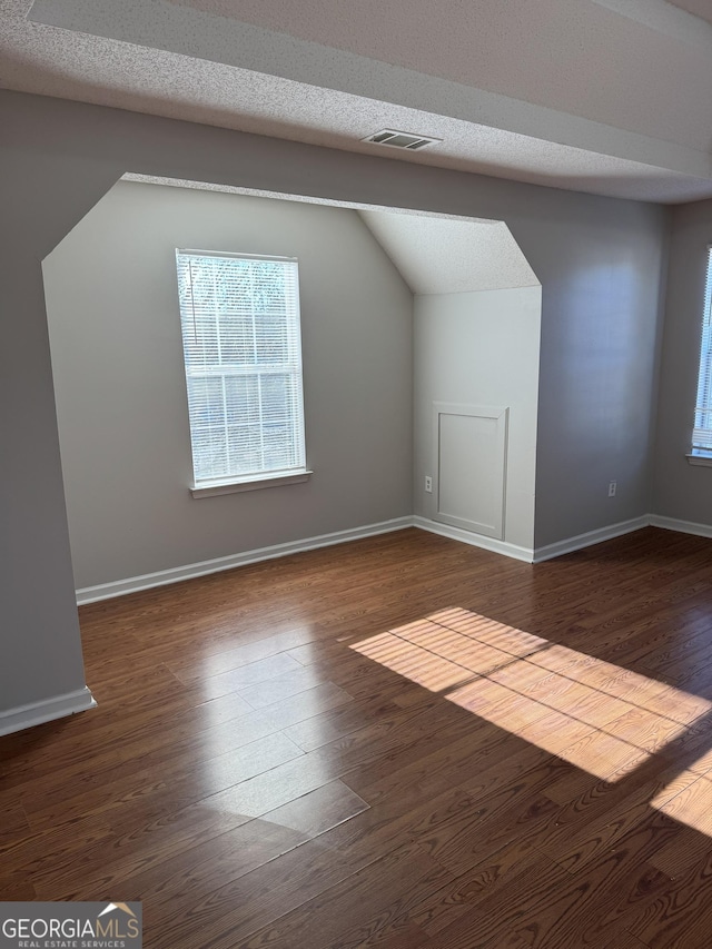 additional living space featuring lofted ceiling, dark hardwood / wood-style floors, and a textured ceiling