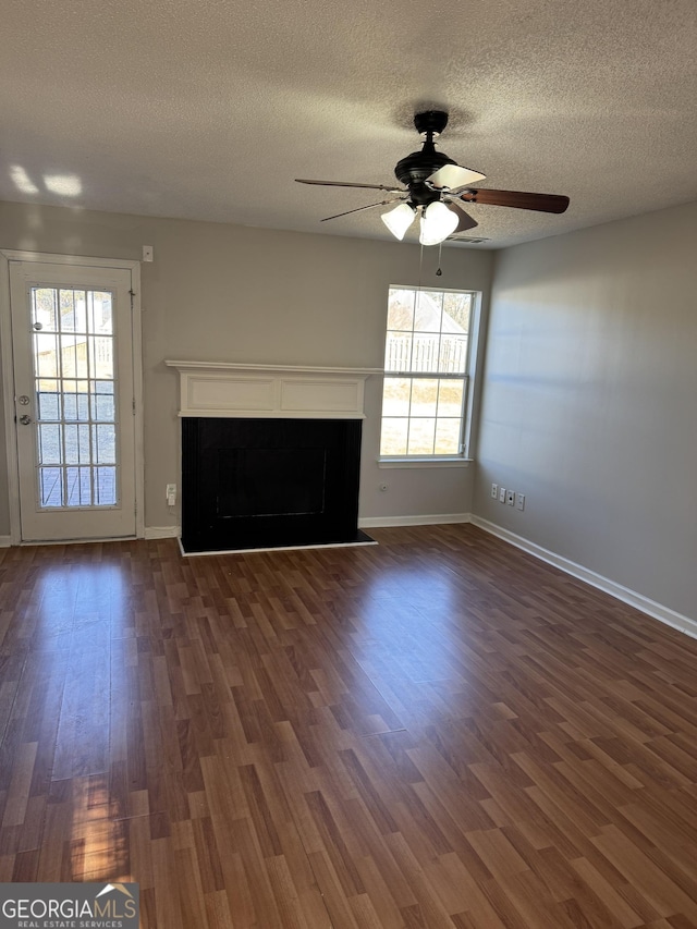 unfurnished living room with ceiling fan, dark hardwood / wood-style floors, a wealth of natural light, and a textured ceiling