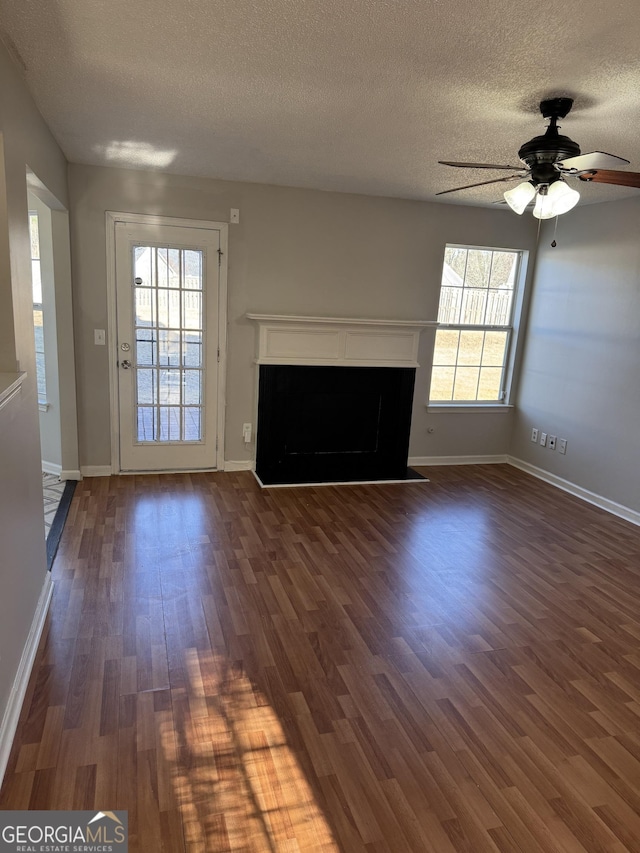 unfurnished living room with ceiling fan, dark wood-type flooring, and a textured ceiling