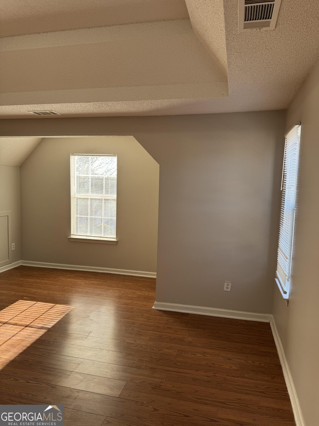 additional living space with dark hardwood / wood-style flooring, vaulted ceiling, and a textured ceiling