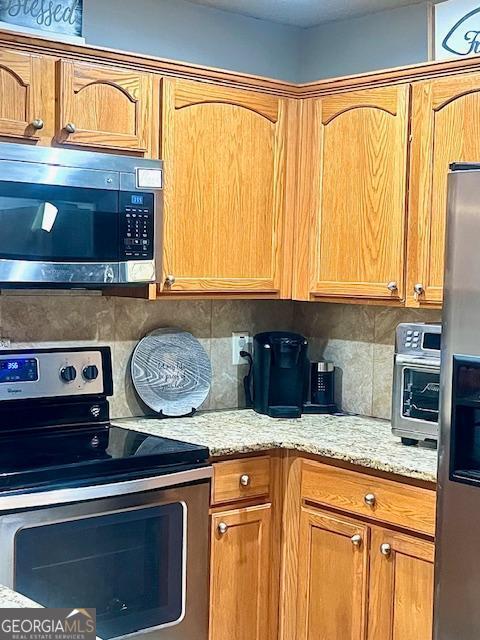 kitchen featuring tasteful backsplash, light stone countertops, and appliances with stainless steel finishes