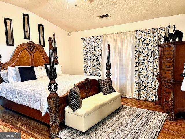 bedroom with hardwood / wood-style flooring, vaulted ceiling, and a textured ceiling